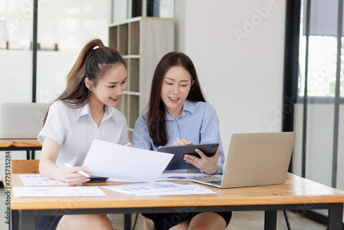 Two young asian business workers using touchpad reading document working at office.