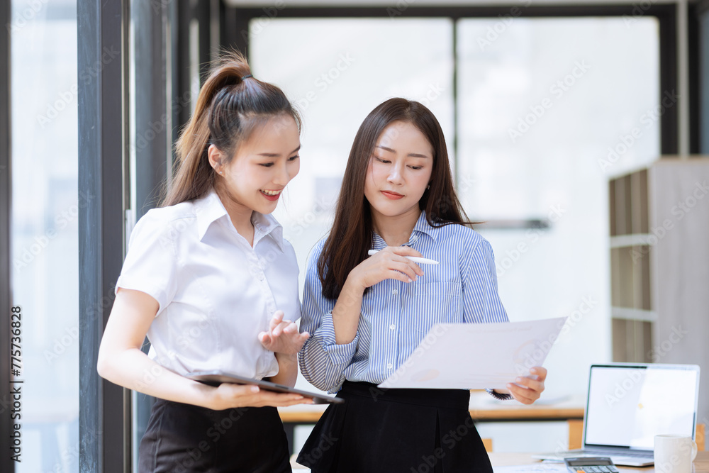 Two young asian business workers using touchpad reading document working at office. Two young asian business workers using touchpad reading document working at office.