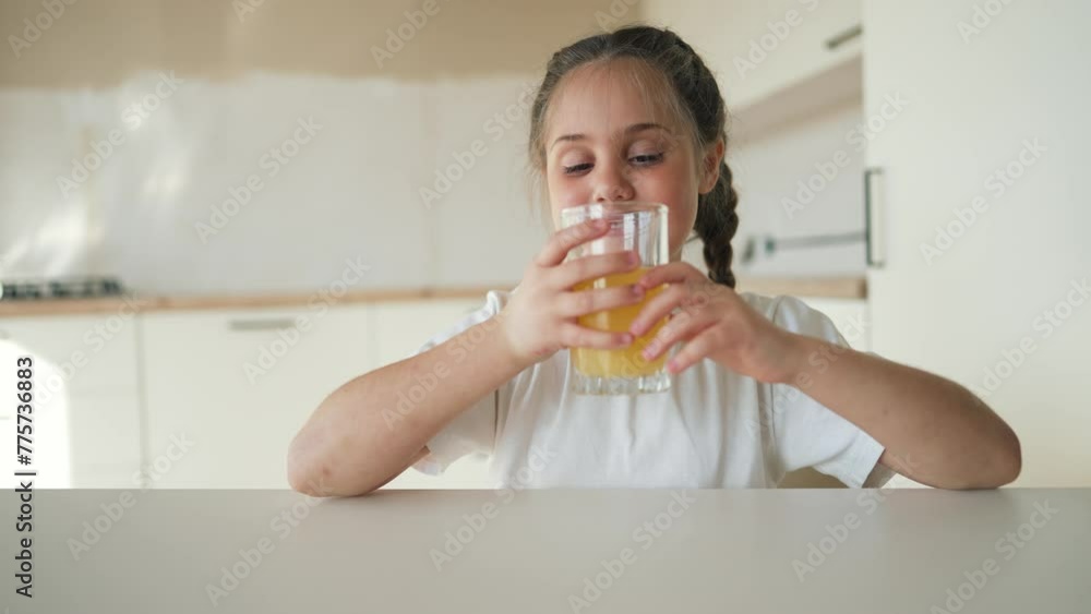 Little cute girl drinks fresh fruit juice. Happy child drinking orange drink. Healthy breakfast for a child. Girl drinks orange juice at the table in the kitchen. Healthy drink for a healthy lifestyle Little cute girl drinks fresh fruit juice. Happy child drinking orange drink. Healthy breakfast for a child. Girl drinks orange juice at the table in the kitchen. Healthy drink for a healthy lifestyle