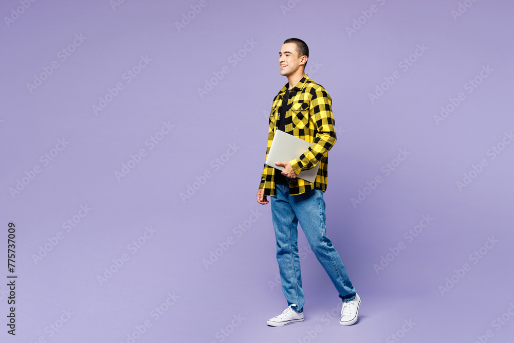Full body side view young IT middle eastern man he wear yellow shirt casual clothes hold closed laptop pc computer isolated on plain pastel light purple background studio portrait. Lifestyle concept. Full body side view young IT middle eastern man he wear yellow shirt casual clothes hold closed laptop pc computer isolated on plain pastel light purple background studio portrait. Lifestyle concept.