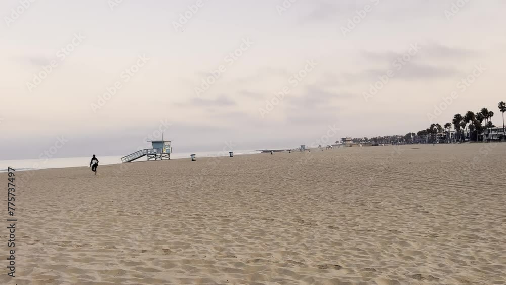Surfer With Surfboard Running On Sandy Shore Towards Sea In Venice Beach, California. wide shot Surfer With Surfboard Running On Sandy Shore Towards Sea In Venice Beach, California. wide shot