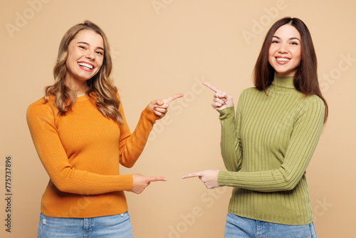 Young friends two women they wears orange green shirt casual clothes together point finger on each other, area between them isolated on plain pastel light beige background studio. Lifestyle concept.