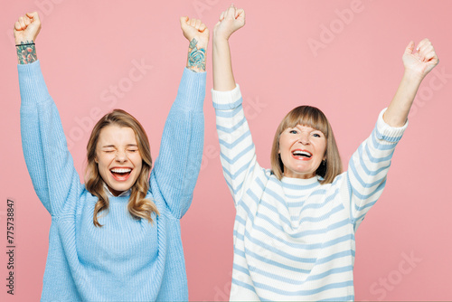 Elder happy parent mom 50s years old with young adult daughter two women together wearing blue casual clothes do winner gesture close eyes isolated on plain pastel pink background. Family day concept.