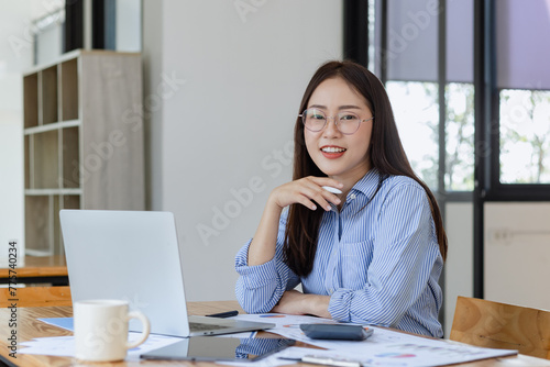 Asian businesswoman working with digital laptop computer and document management at desk in office.