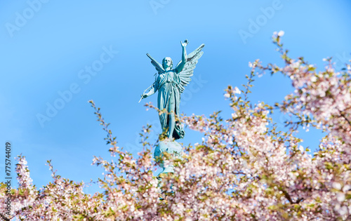 Angelic statue for the fallen in war saluting high on a column above blooming pink cherry flowers commemorates the death of Admiral Ivar Huitfeldt (1886) in a Naval Battle or war. Copenhagen, Denmark
