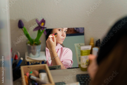 Teenage girl putting on makeup in front of a mirror