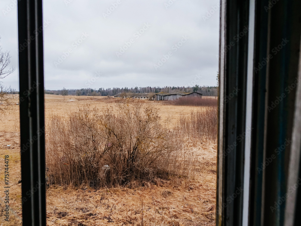 View from a window of a farm house on dark and moody nature after winter. Abandoned milk farm building in the background. Living in a county side. View from a window of a farm house on dark and moody nature after winter. Abandoned milk farm building in the background. Living in a county side.