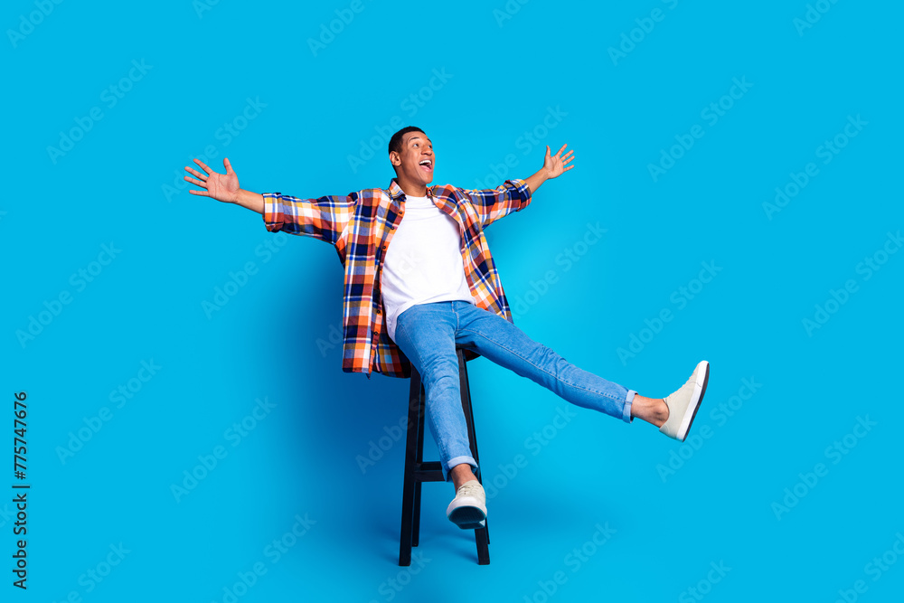 Full length photo of nice young man sit chair look empty space wear shirt isolated on blue color background