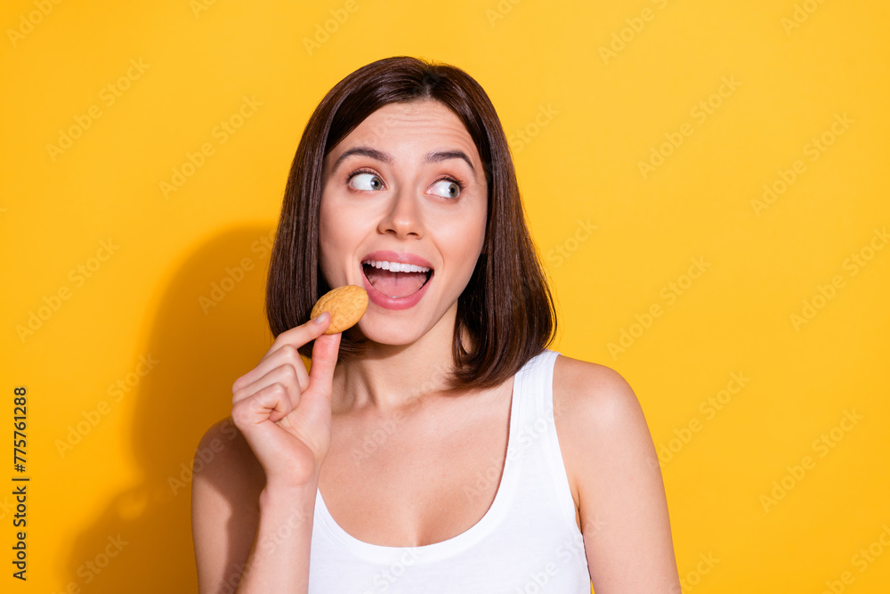 Photo portrait of attractive young girl hold bite cookies look empty space wear trendy white outfit isolated on yellow color background