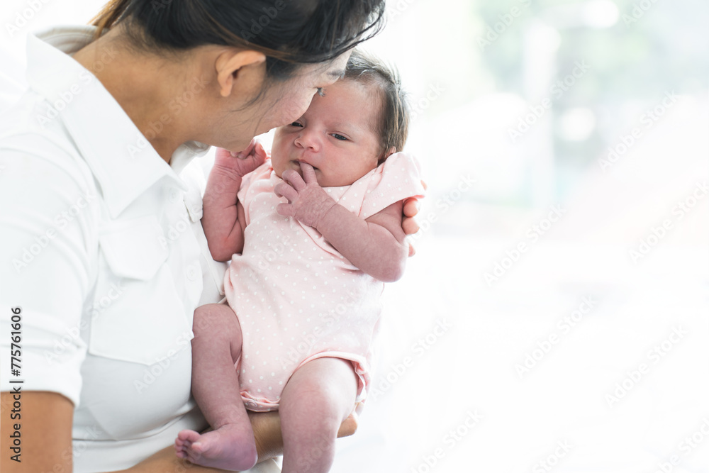 Mother carrying and kissing her newborn baby girl at home. Cute 19 days Asian Australian infant baby lean in mom arms. Parent and little kid relaxing at home. Family and child care concept