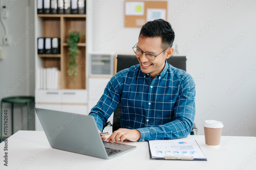 Young handsome man typing on tablet and laptop while sitting at the working table office Young handsome man typing on tablet and laptop while sitting at the working table office