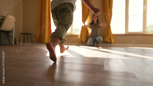 Happy family. Baby feet walk on floor towards mother. Child makes steps barefoot on parquet floor in children room. Son runs to his mother on the laminate with his bare feet. happy baby first steps photo
