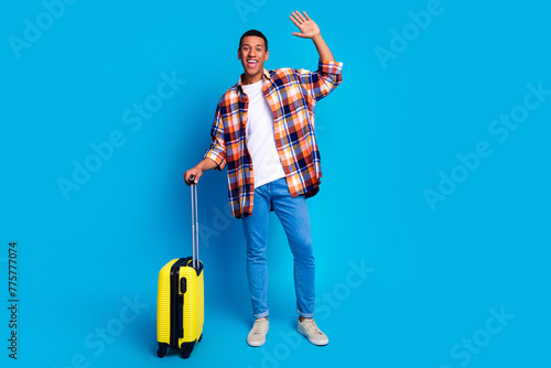 Full size portrait of nice young man suitcase arm wave hi empty space wear shirt isolated on blue color background