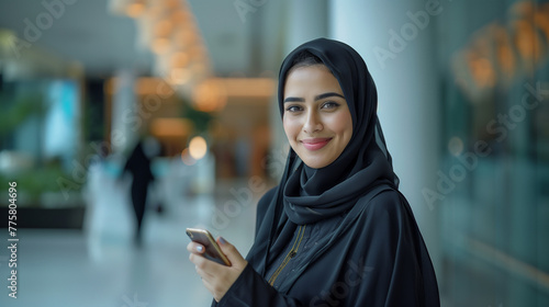 A smiling Arab Emirati businesswoman Wearing UAE Emirati Traditional Dress, black abaya, stands in her office, Speaking In mobile phone, Arabian Woman in the Emirates, generative ai. photo
