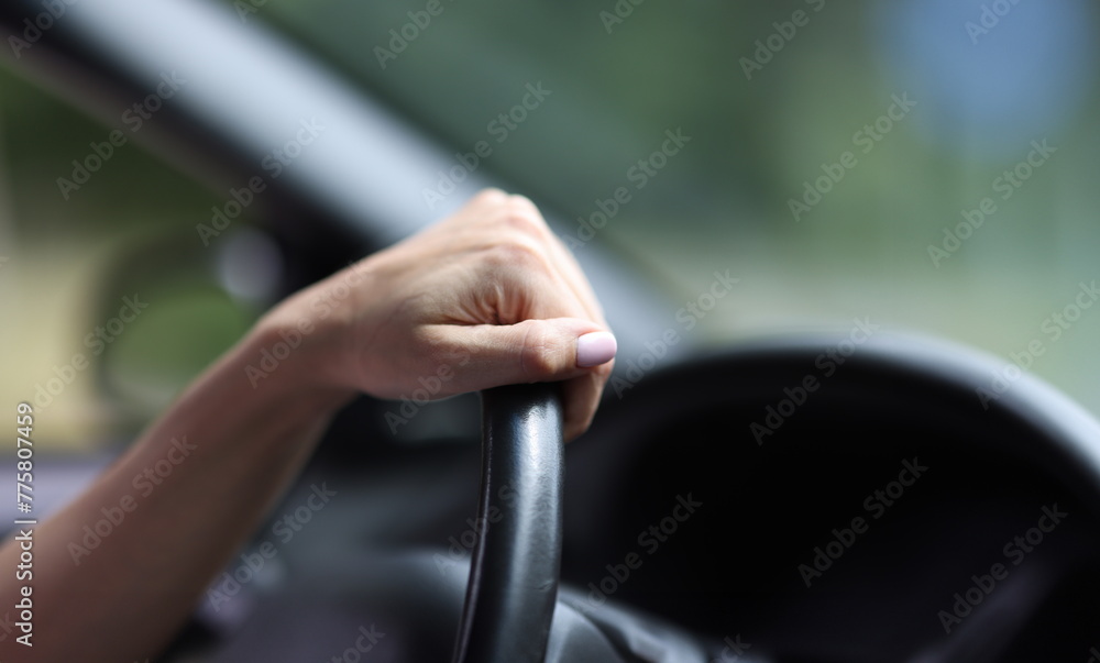 Female hand hold leather steering wheel in car. Driving training.