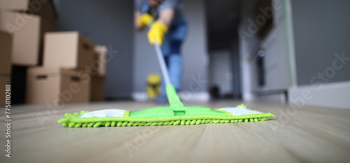 Male hand with yellow protective gloves hold green plastic mop close-up. Cleaning after repair concept photo