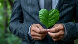Corporate responsibility concept with businessman holding heart-shaped leaf.