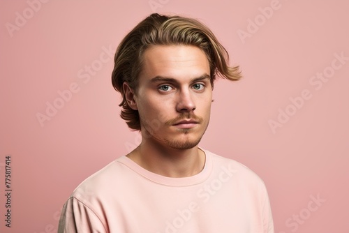A man with a beard and a pink shirt is standing in front of a pink background
