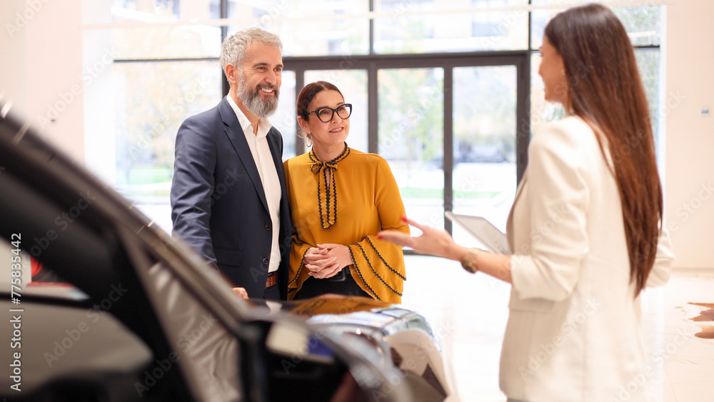 Young saleswoman recommending a car to a mature couple Young saleswoman recommending a car to a mature couple