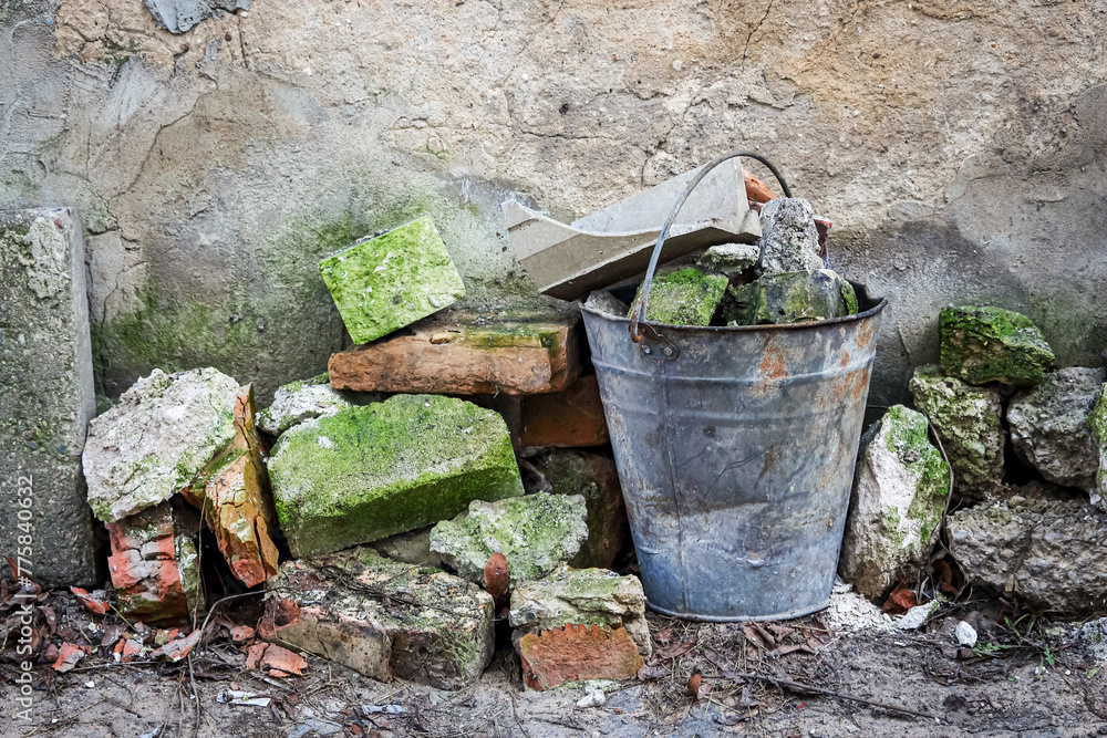 Old metal bucket among aged bricks with green moss on abandoned construction site Old metal bucket among aged bricks with green moss on abandoned construction site