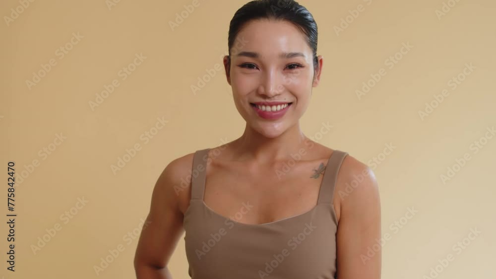 Tilt up portrait of Asian sporty woman in beige sportswear posing for camera against yellow wall background Tilt up portrait of Asian sporty woman in beige sportswear posing for camera against yellow wall background