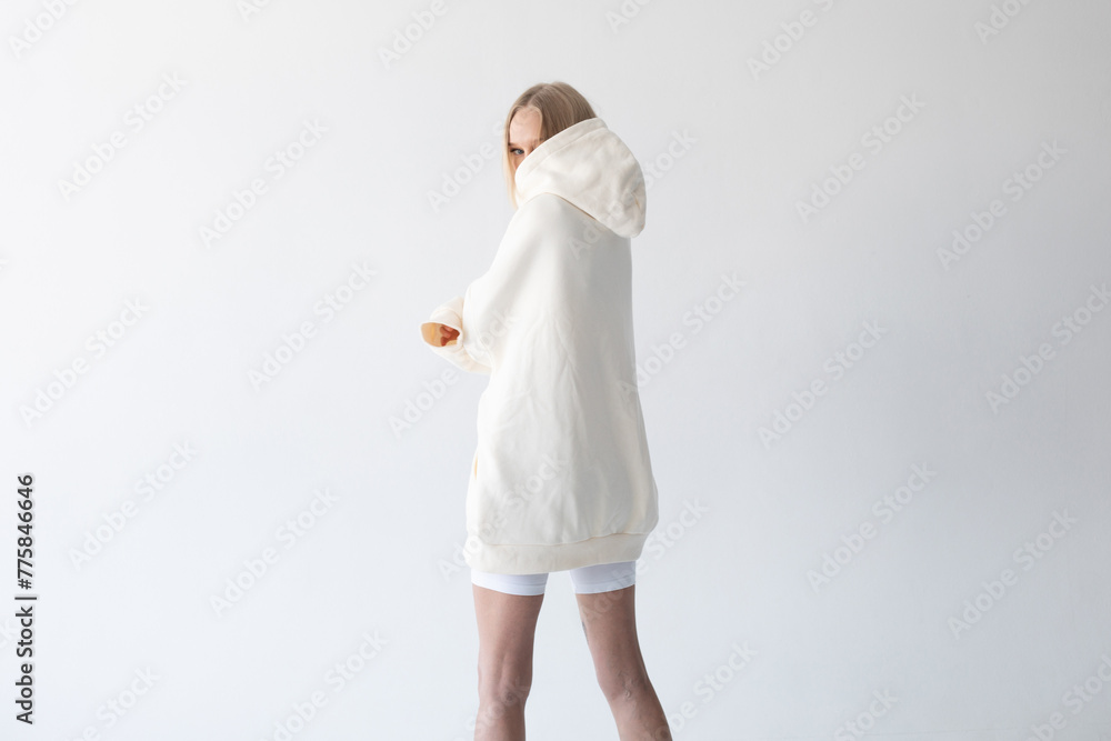 Beautiful blonde woman posing in white hoodie and leggings posing against white background. Posing with his back. Beautiful blonde woman posing in white hoodie and leggings posing against white background. Posing with his back.