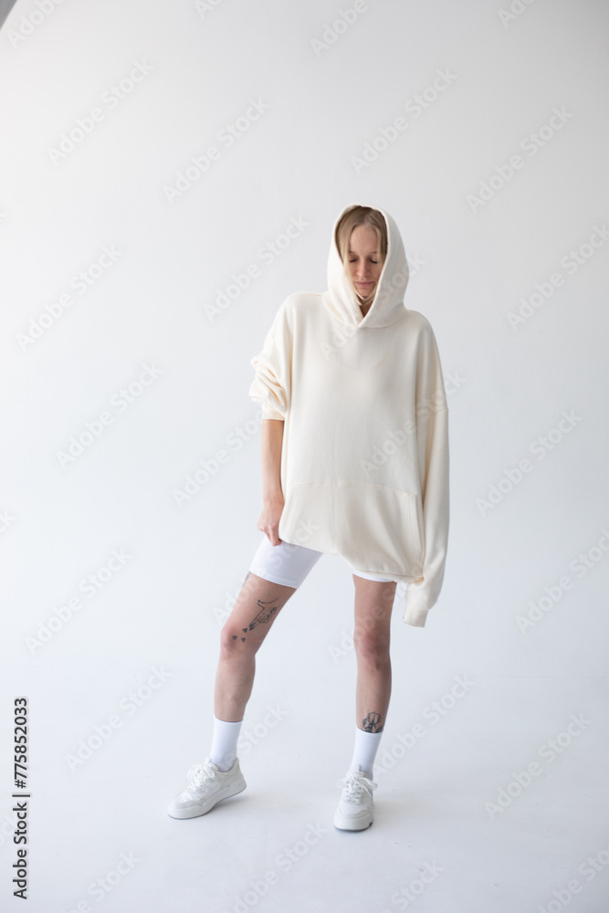 Beautiful blonde woman posing in white hoodie and leggings posing against white background Beautiful blonde woman posing in white hoodie and leggings posing against white background