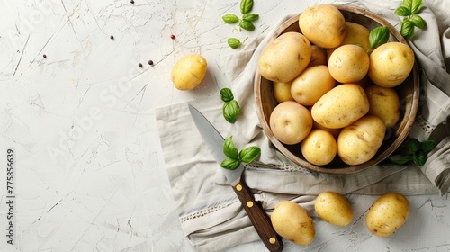 Bowl with raw potatoes and knife on light background.