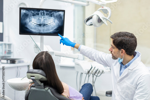 Professional male dentist showing x-ray footage of teeth to female patient in clinic office