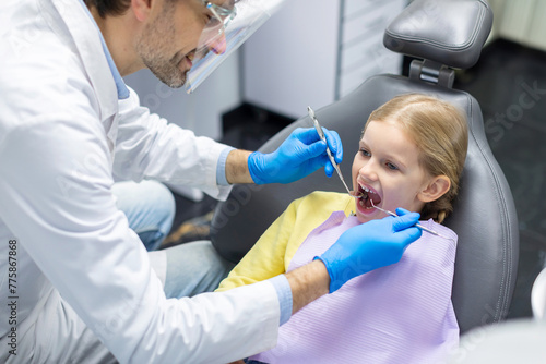 Little girl patient sitting on dental chair in dentists office on her regular checkup for caries and gum disease