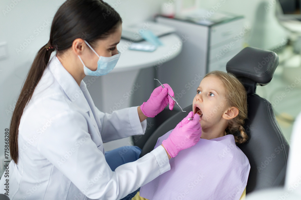 Young female doctor treats tooth of little girl at dentist's clinic, making checkup of caries for female patient Young female doctor treats tooth of little girl at dentist's clinic, making checkup of caries for female patient