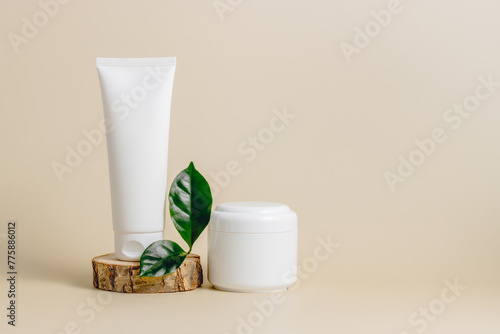 Mockup unbranded cream tube with cream bottle on wooden podium with green leaf  copy space. Skincare beauty product container template for design. Natural organic skincare