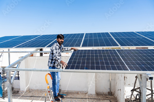 Indian worker installing solar panels on roof of house. Maintenance of photovoltaic panel system. Concept of alternative, renewable energy.