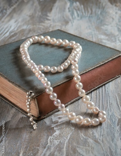 A delicate pearl necklace draped over an aged leather-bound book on an old wooden table, suggesting a story of timeless elegance