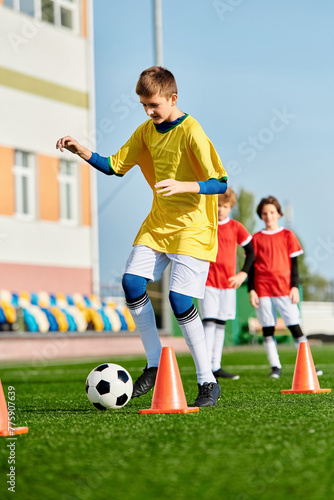 A lively group of young boys kicking a soccer ball around cones on a vibrant field, showcasing teamwork and skill in action. © LIGHTFIELD STUDIOS