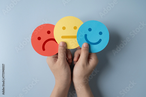paper cut smiley face, stressed and sad in hands on light blue background. positive thinking, assessment and world mental health day.