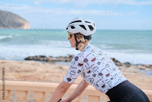 Beautiful woman cyclist wearing cycling kit and helmet riding a bicycle near the sea with amazing view. Calpe, Alicante, Spain.