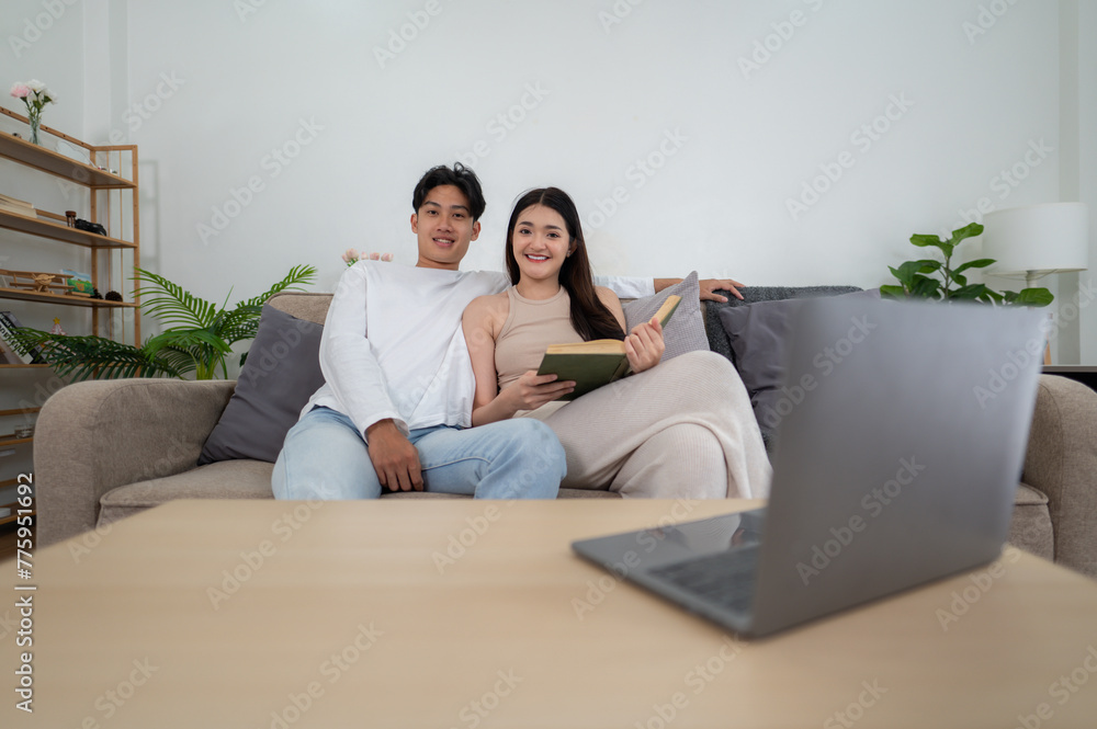 A happy Asian couple shares a moment reading a book together with a laptop, blend of traditional and digital pastimes. A happy Asian couple shares a moment reading a book together with a laptop, blend of traditional and digital pastimes.