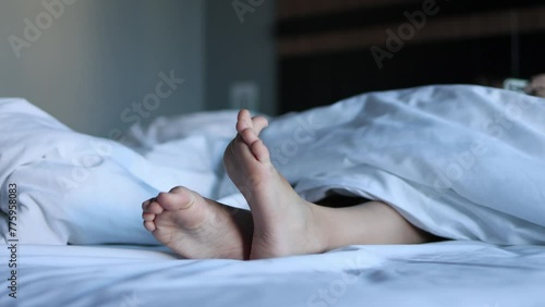 The view of a child's legs sticking out from under a blanket lying on a large snow-white bed illustrates the concept of sleep and peace.