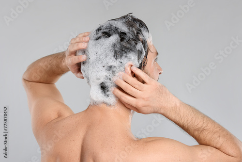 Man washing his hair with shampoo on grey background, back view