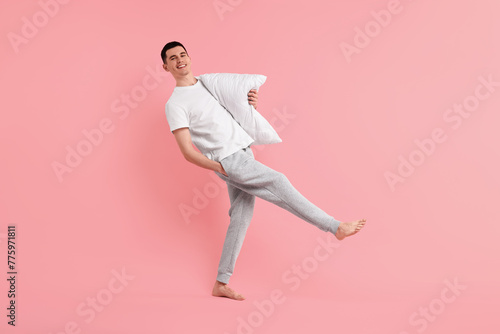 Happy man in pyjama holding pillow on pink background