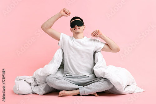 Happy man in pyjama with sleep mask and blanket on pink background © New Africa