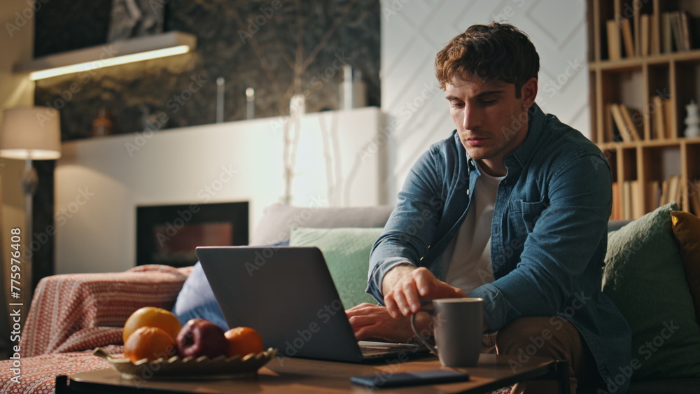 Fototapeta premium Focused freelancer typing laptop sitting couch living room late evening close up