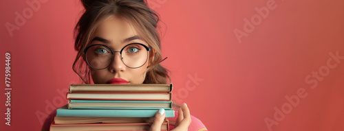 A girl with red hair and glasses is holding a stack of books. Concept of studiousness and determination. A librarian with glasses holding a stack of books, looking knowledgeable on a bright background photo