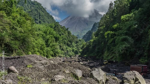 Yogyakarta, Indonesia - February 11, 2024. Morning activity of sand mining in the Boyong River with Merapi Mount in the background. Miners load the sand into trucks, then it is delivered to the buyer. photo