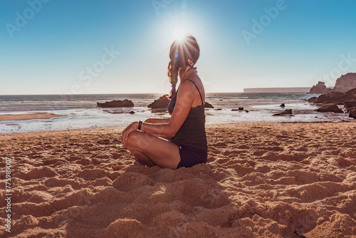 Ragazza seduta a gambe incrociare sulla riva del mare con il sole contro luce