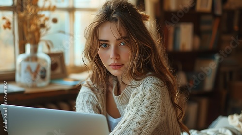 A young woman with captivating eyes works on her laptop in a cozy, sunlit room 