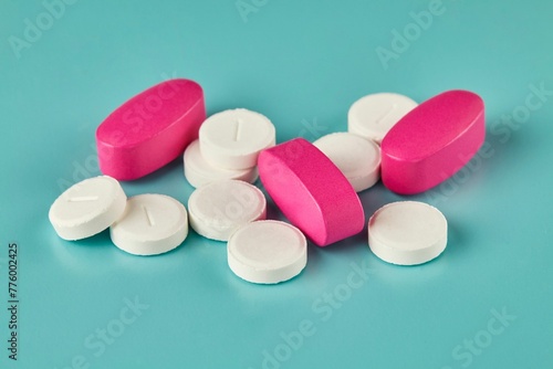 Closeup shot of medicine white tablets and pink caplets on the cyan background photo