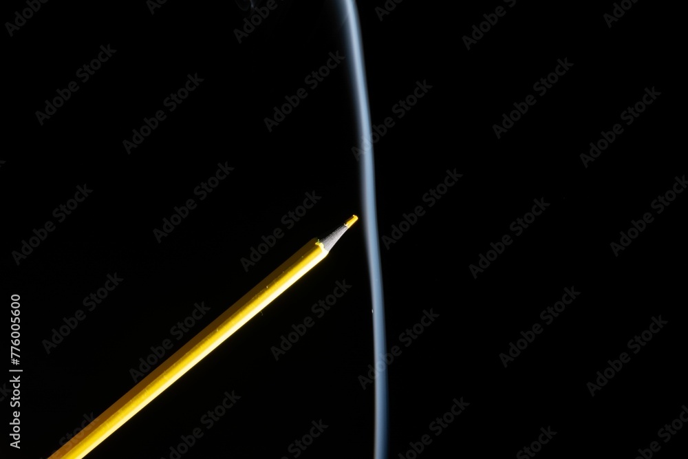 Closeup of yellow colored pencil touching the white smoke coming from below, with copy space. Closeup of yellow colored pencil touching the white smoke coming from below, with copy space.