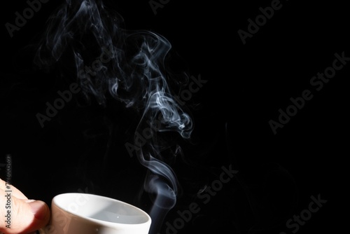 Hand holding a white cup with smoke against a black background